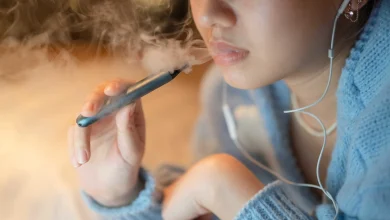 مراهق يدخن سيجارة إلكترونية في الشارع، مما يعكس انتشار استخدام السجائر الإلكترونية بين الشباب في الأماكن العامة.