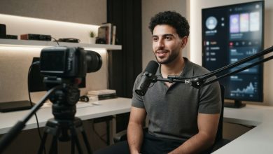 شاب صانع محتوى رقمي أمام كاميرا احترافية داخل استوديو حديث مع تجهيزات التصوير وشاشات التواصل الاجتماعي