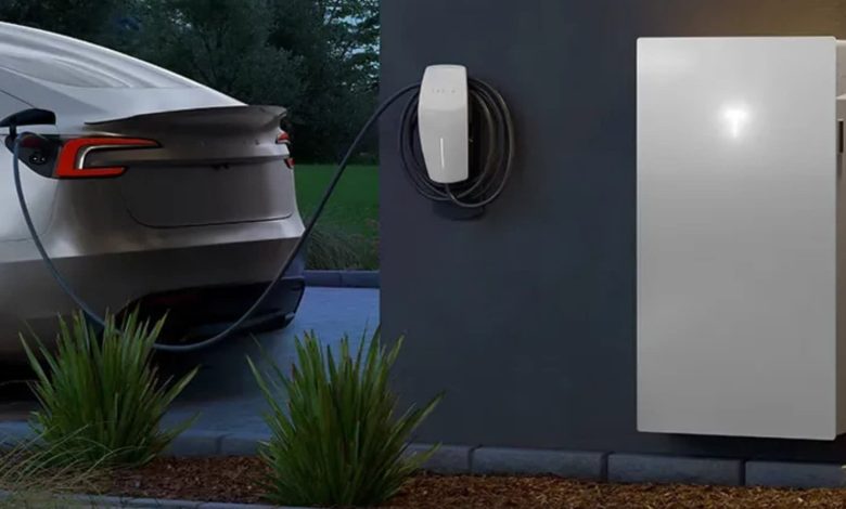 سيارة Tesla Model 3 متوقفة بجوار منزل حديث مزود بوحدات Powerwall 3 ونظام شحن، في مشهد يوضح استخدام بطارية السيارة كمصدر للطاقة الاحتياطية للمنزل.