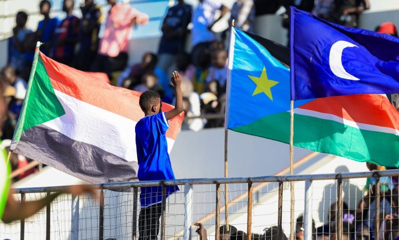 مشهد من مدرجات مباراة الهلال السوداني وجاموس الجنوب سوداني في جوبا، حيث يرفع طفل أعلام السودان وجنوب السودان والهلال في أجواء جماهيرية مميزة.