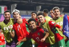 صورة جماعية لمنتخب المغرب للشباب يحتفلون بالتأهل في الملعب، واللاعبون يرفعون الأيدي فرحًا بالانتصار.
