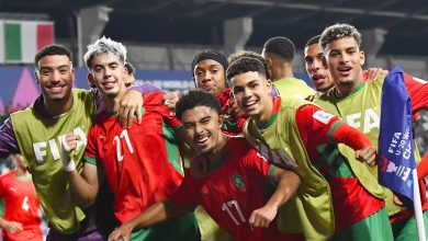 صورة جماعية لمنتخب المغرب للشباب يحتفلون بالتأهل في الملعب، واللاعبون يرفعون الأيدي فرحًا بالانتصار.