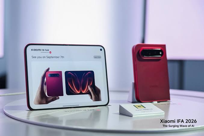 "هاتف Xiaomi 18 Fold القابل للطي الأحمر في معرض Xiaomi IFA 2026 مع لوحة إعلانية تعرض تاريخ الإطلاق."