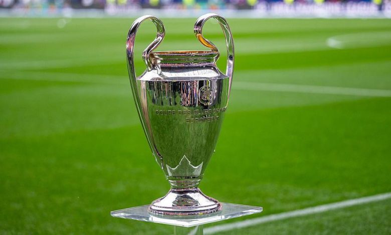 كأس بطولة دوري أبطال أوروبا اللامع موضوع على قاعدة شفافة داخل أرضية الملعب الخضراء.