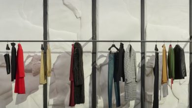 مشهد واقعي لعرض أزياء Gucci في ميلانو داخل متجر فاخر تحول إلى منصة عرض، مع عارض أزياء رجل يقف في المنتصف محاطًا بالحقائب والأحذية والإكسسوارات الفاخرة وسط أجواء أسبوع الموضة في ميلانو.