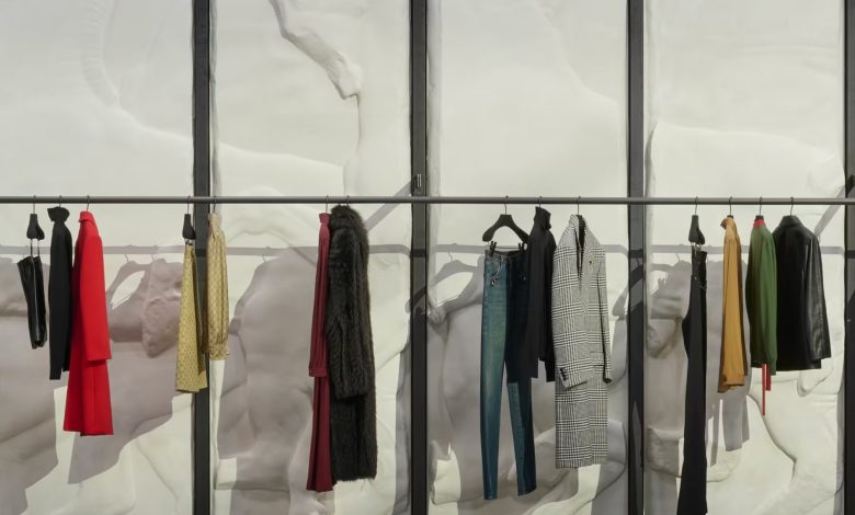 مشهد واقعي لعرض أزياء Gucci في ميلانو داخل متجر فاخر تحول إلى منصة عرض، مع عارض أزياء رجل يقف في المنتصف محاطًا بالحقائب والأحذية والإكسسوارات الفاخرة وسط أجواء أسبوع الموضة في ميلانو.